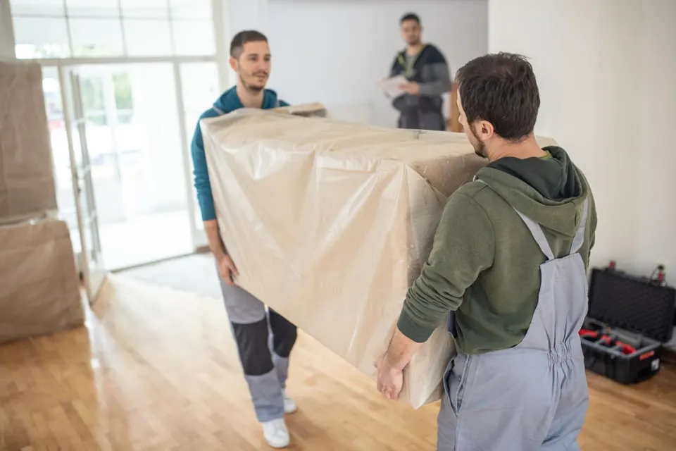 Équipe Devis Débarras portant un meuble emballé dans un appartement
